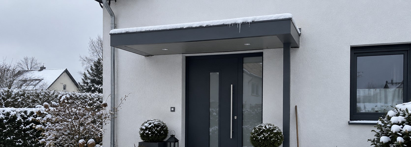 Haustür-Vordach in Anthrazit mit Schnee und kleinen Eiszapfen über einem Hauseingang im Winter – Deutsche Kunststoffbedachungen