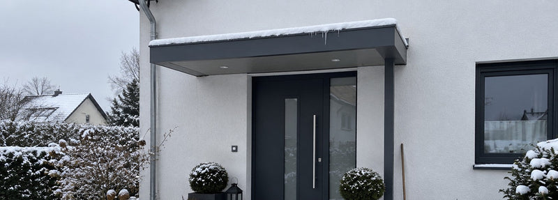 Haustür-Vordach in Anthrazit mit Schnee und kleinen Eiszapfen über einem Hauseingang im Winter – Deutsche Kunststoffbedachungen