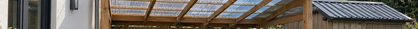 Holz-Carport mit klaren Kunststoff-Wellplatten neben einem Schuppen mit Trapezblech – Deutsche Kunststoffbedachungen